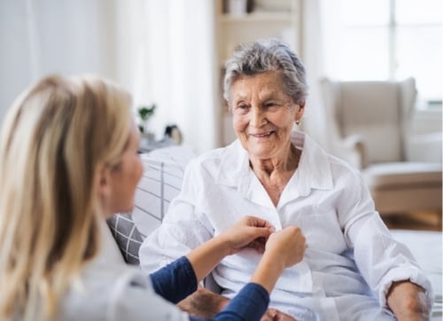 Nurse helping an smiling elderly lady get dressed