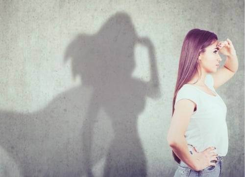 Woman standing looking in the distance and her shadow is a super woman with a cape