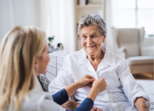 Nurse buttoning a blouse of a smiling elderly lady